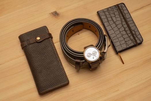 Men's accessories with brown leather wallet, belt, notebook and watch on wooden background