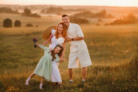 A beautiful happy family of three is standing in a field at sunset.