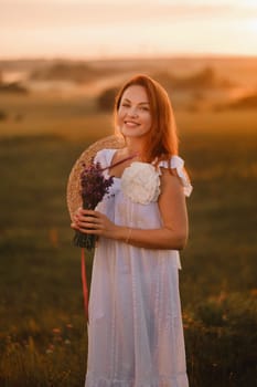 A girl in a white dress with a bouquet of lavender flowers stands in a field at sunset.
