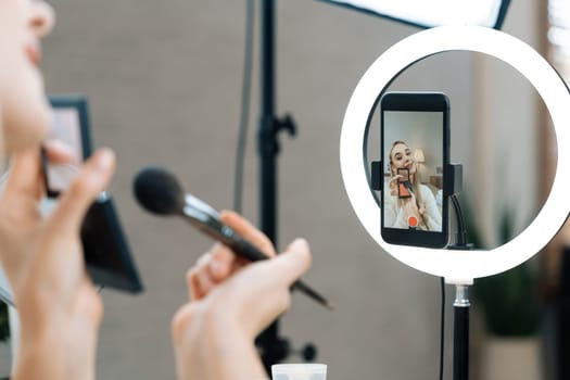 Rear view young woman making beauty and cosmetic tutorial video content for social media. Beauty blogger showing how to apply beauty care to audience or follower on camera screen. Blithe