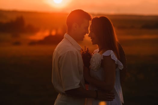 A couple in love in white clothes in a field at a red sunset.