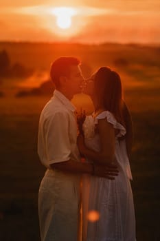 A couple in love in white clothes in a field at a red sunset.