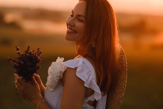 A girl in a white dress with a bouquet of lavender flowers stands in a field at sunset.