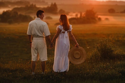 A couple in love in white clothes in a field at a red sunset.