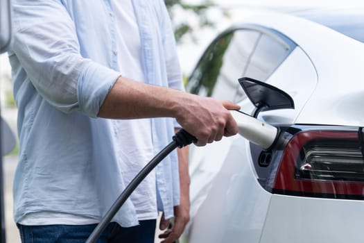 Eco-friendly conscious man recharging modern electric vehicle from EV charging station. EV car technology utilized as alternative transportation for future sustainability. Synchronos