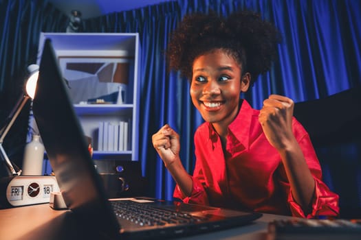 African woman blogger wearing pink shirt with happy face, looking on screen laptop with valued achievement project or get scholarship. Concept of cheerful expression work from home. Tastemaker.