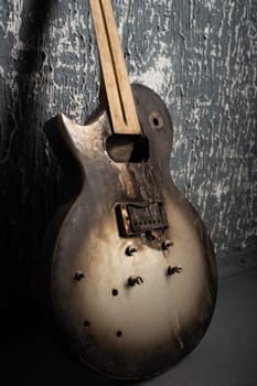 Burnt broken old electric guitar against the background of a dark wall.