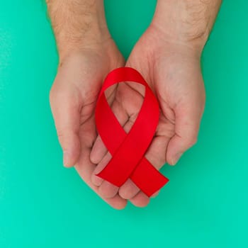 Healthcare and medicine concept - male hands holding red AIDS awareness ribbon