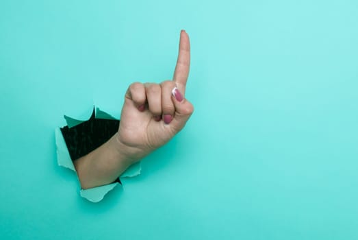 Female hand pointing finger up close-up. Copy space. Torn paper, blue background.