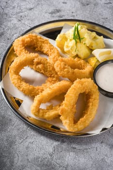 Fried calamari with potato salad next to it on stone table