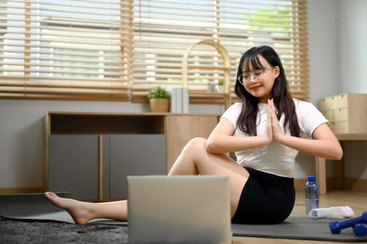 Young Asian woman practice yoga on mat and watching online lessons on laptop.