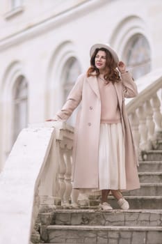 woman in elegant coat and hat against an intricate architectural backdrop, harmoniously blending modern fashion with historical allure. The soft daylight adds to its timeless appeal