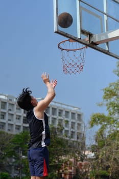 Shot of basketball player throwing a ball toward basket training on the urban basketball court.