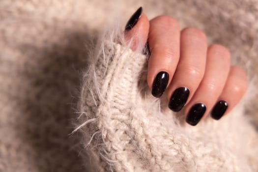 Beautiful female manicure of black color. Woman hand in cashmere knitwear.