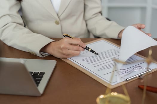 A woman in a business suit is sitting at a desk with a laptop and a piece of paper. She is smiling and she is happy