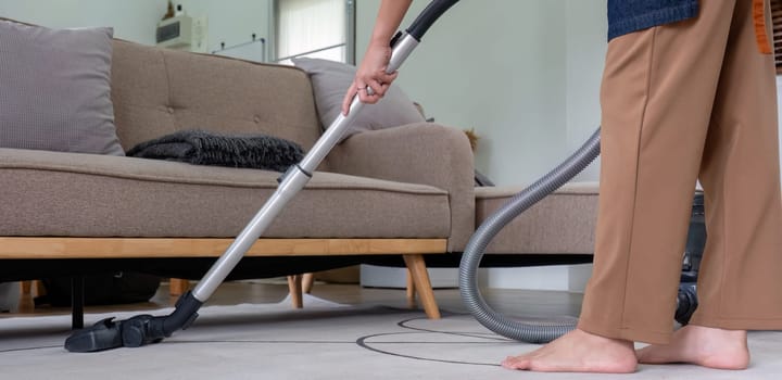 Young housewife is cleaning the living room floor with a vacuum cleaner..