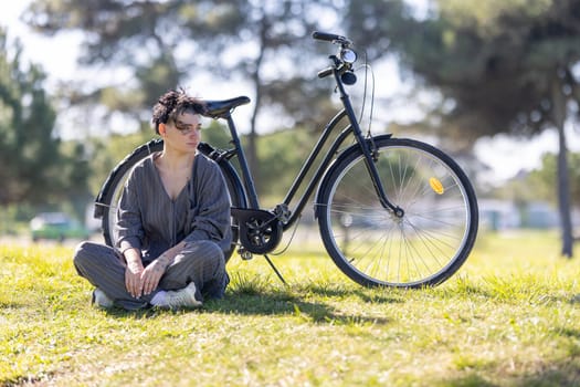 A woman sits on the grass next to a black bicycle, portrait