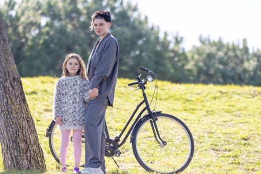 A woman and her daughter little girl are standing next to a bicycle in the park