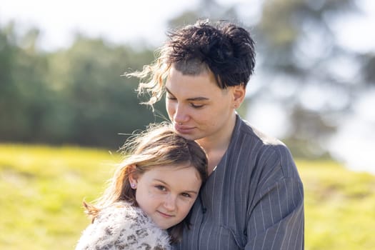 A woman is hugging a young girl. The girl has a nose piercing. The woman is wearing a gray jacket