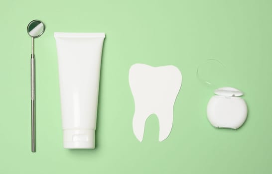 Dental mirror, tube of toothpaste and dental floss on a green background, top view