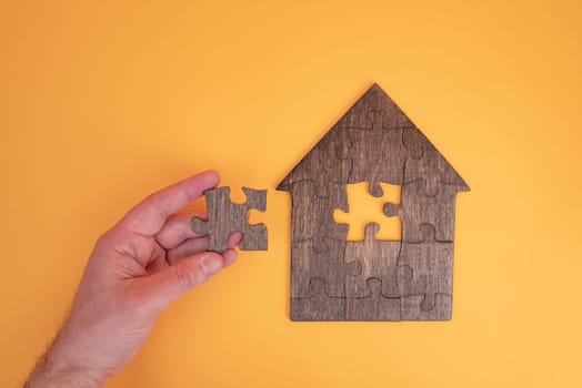 Puzzle house with a missing piece in mans hand. The acquisition or construction comfortable dream home. Mortgage loan purchase real estate. Arrangement premises repair. Availability and cheapness. Finish building