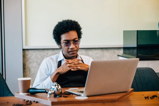 A focused coffee barista and owner meticulously checks beans using a laptop in a modern roastery office. Utilizing technology ensuring top-quality beans. Entrepreneur inspection is thorough.