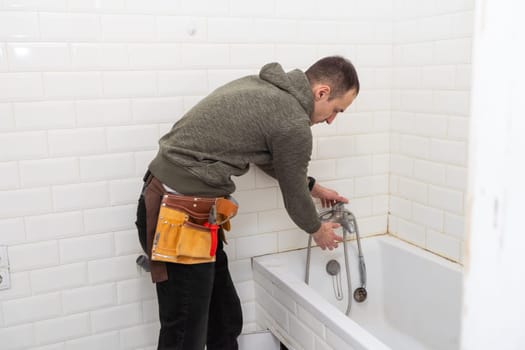 A male plumber with wrench repairs the faucet in the bathroom. replacement and maintenance of plumbing. handyman service. small business. High quality photo