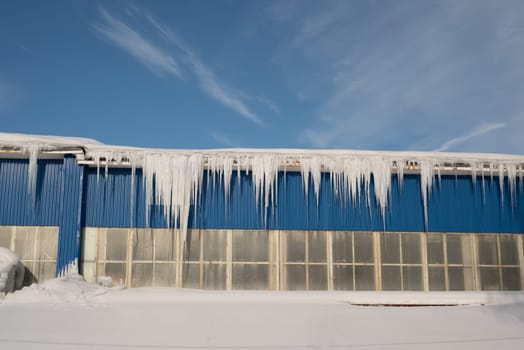 Big icicles on the roof of a townhouse on a snowy winter day among thaw. Cleaning the roofing from snow and icicles.