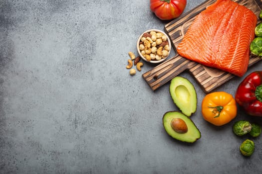 Fresh raw salmon fillet on wooden cutting board, organic bio vegetables and nuts on rustic stone grey background top view. Ingredients full of vitamins for healthy diet and nutrition, space for text