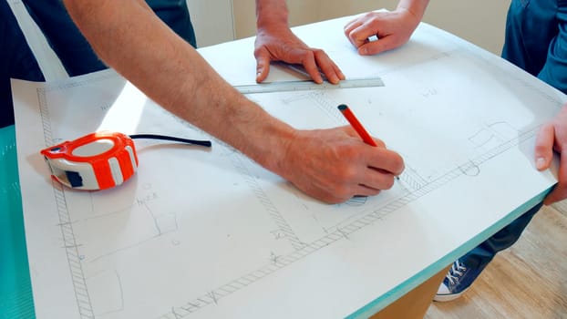 Two workers are developing a scheme of the house. The project is drawn on paper.