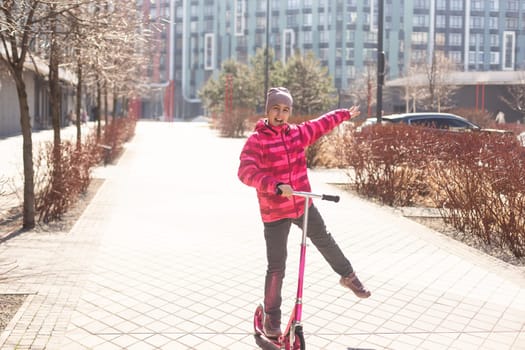 Little cute girl riding a scooter on a path in the park. High quality photo
