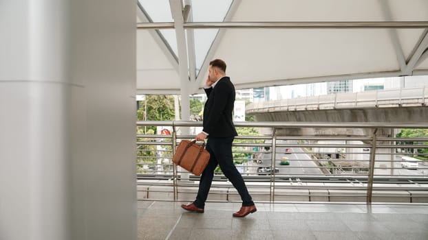 Smart caucasian businessman calling his colleague to plan financial strategy while walking to workplace. Side view of manager using mobile phone to communicate with marketing team. Lifestyle. Urbane.