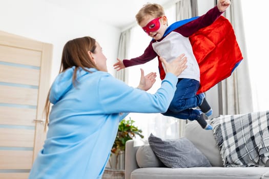 Mother playing with child in superhero costume. Indoor leisure activity concept. Design for parenting, family fun