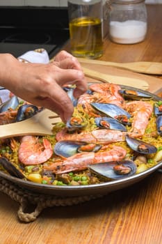 Hand serving shrimp and mussel paella with a wooden spoon from a pan, typical Spanish cuisine, Majorca, Balearic Islands, Spain,