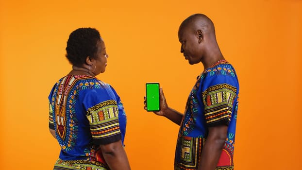 African american couple looking at greenscreen on phone layout, using isolated chromakey template on display. Man and woman pointing at blank copyspace mockup mobile phone screen.