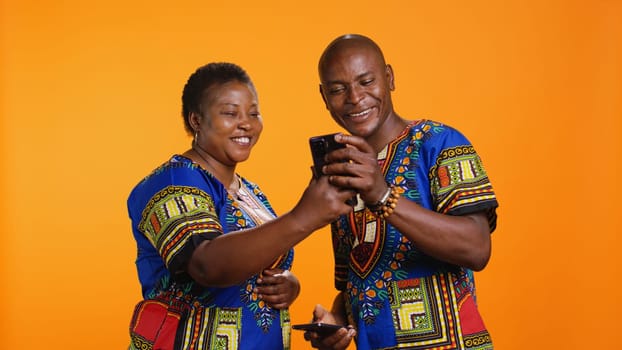 African american couple checking social media network on smartphone app, reading their messages on internet connection. Man and woman using mobile phone to scroll on websites.
