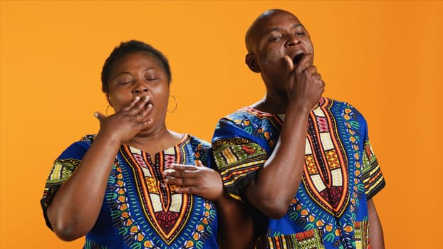 Sleepy african american people yawning in front of camera, feeling extremely tired over orange background. Man and woman being exhausted and dealing with burnout, overworked persons.