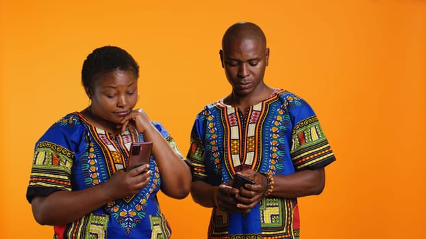 Ethnic people in traditional clothes checking smartphone apps, looking at messages received on social media network. African american man and woman browsing websites on mobile device.