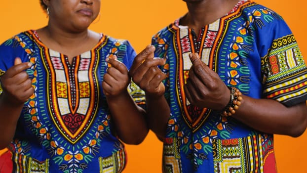 Serious husband and wife asking for salary in studio, rubbing their fingers to ask for cash payment or loan. Ethnic people in poverty demanding money income, financial difficulties. Close up.