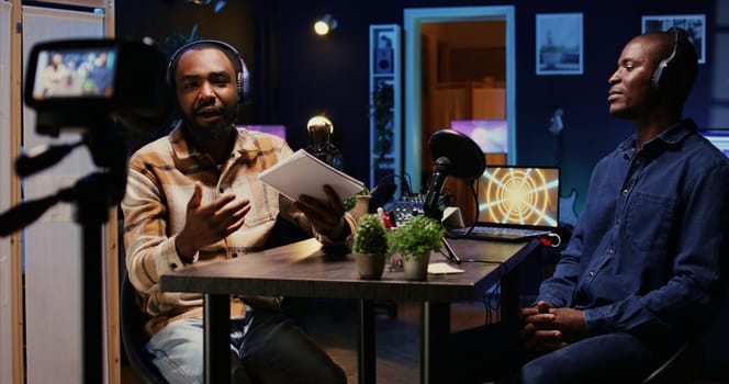 Cohosts streaming podcast using professional vlogging gadgets to live broadcast debate on politics vlog channel. Men meeting in neon lights decorated living room studio to film show