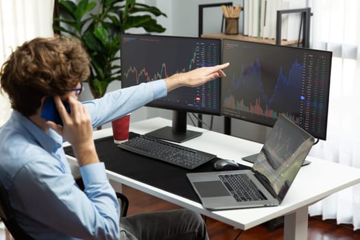 Successful young investor stock trader calling on smartphone to business partner with dynamic financial exchange investment laptop screen in current market graph in real time at modern office. Gusher.