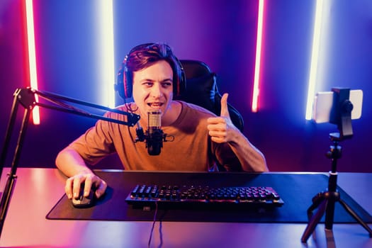 Host channel of gaming smart streamer playing online game, wearing headphone with viewers live steaming on media social online by smartphone talking with team player at neon lighting room. Pecuniary.