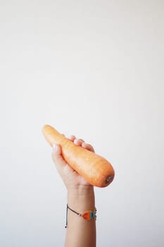 A child is holding a carrot as a food ingredient in their hand.