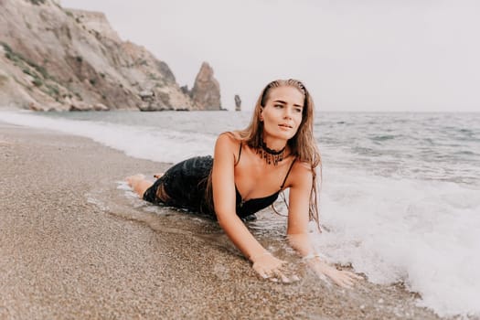 Woman travel sea. Young Happy woman in a long red dress posing on a beach near the sea on background of volcanic rocks, like in Iceland, sharing travel adventure journey