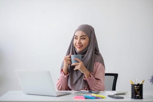 Smiling Muslim business woman Wearing a hijab while chatting online on a work desk in the office..