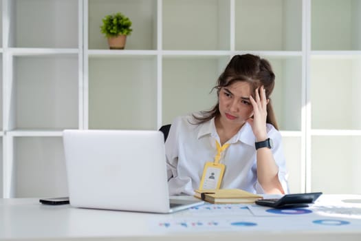 Asian businesswoman who is tired and has a headache from difficult work causing stress Sitting and looking at work at the desk in the office..