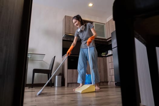 A beautiful young woman wear orange rubber gloves and sweep the floor while listening to music while wearing headphones..