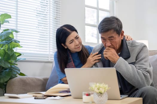 Retired Asian couple in their 60s Feeling stressed while calculating monthly expenses on the living room sofa..