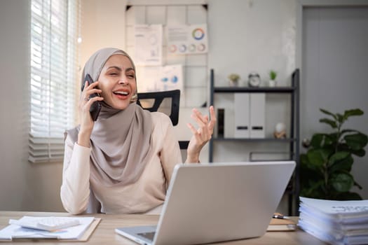 Happy Muslim businesswoman wearing hijab at work Use your laptop and smartphone to work on finance and marketing in the office..