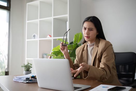 Asian businesswoman feeling tired and stressed over an unsuccessful business while working in a home office decorated with soothing green plants..